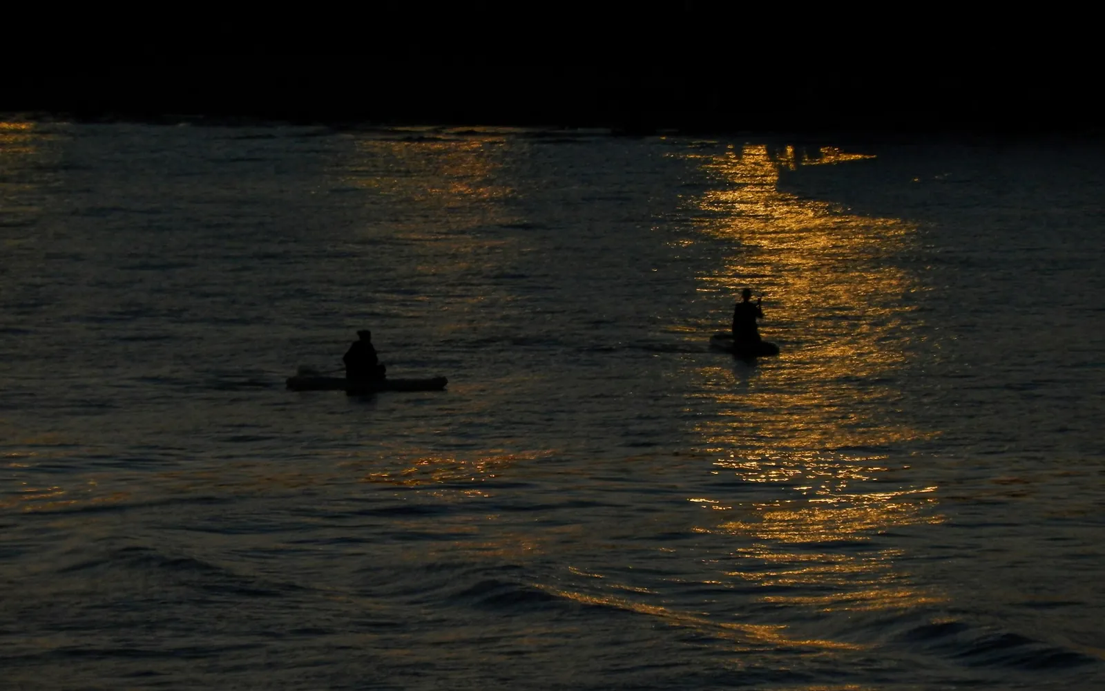 Two paddlers crossing a still lake in the last of the evening light