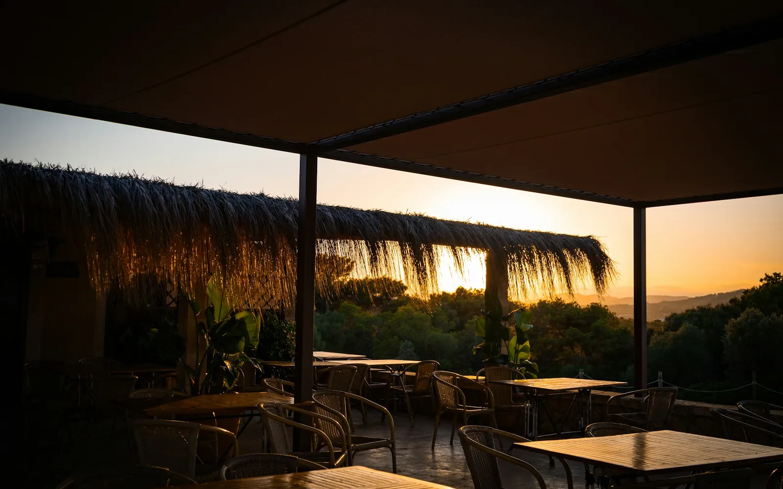 Tables laid on a covered restaurant terrace looking out over hills at golden hour
