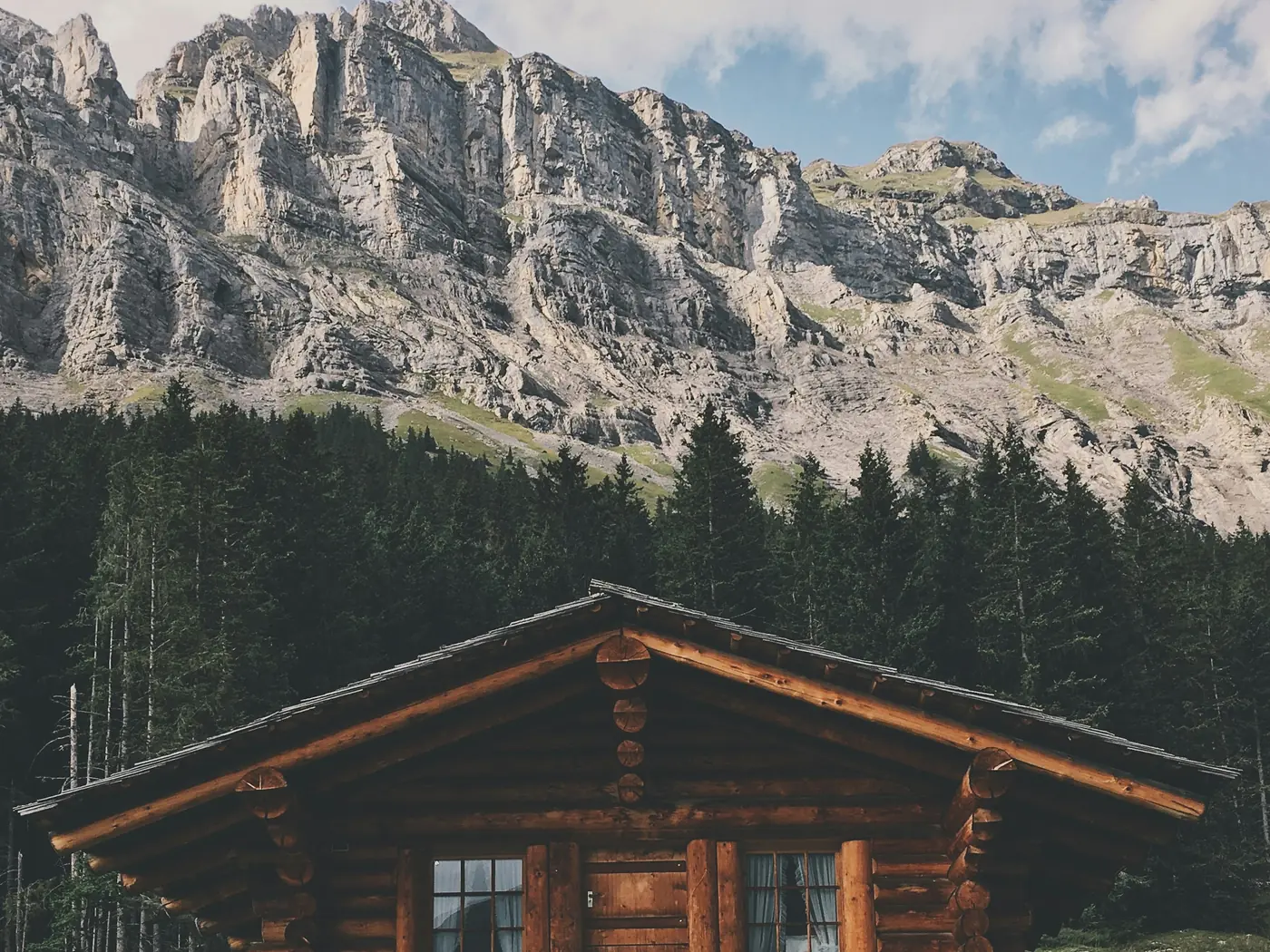 A log cabin with a timber balcony below a limestone mountain face