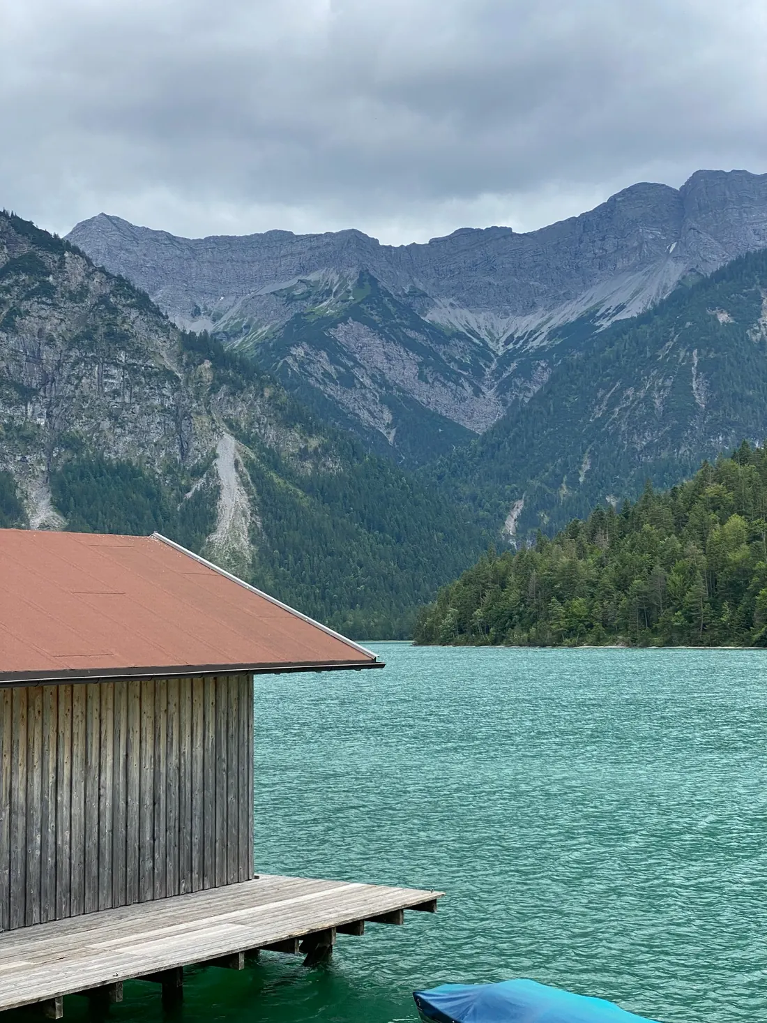 A timber boathouse and jetty on a still alpine lake below the mountains