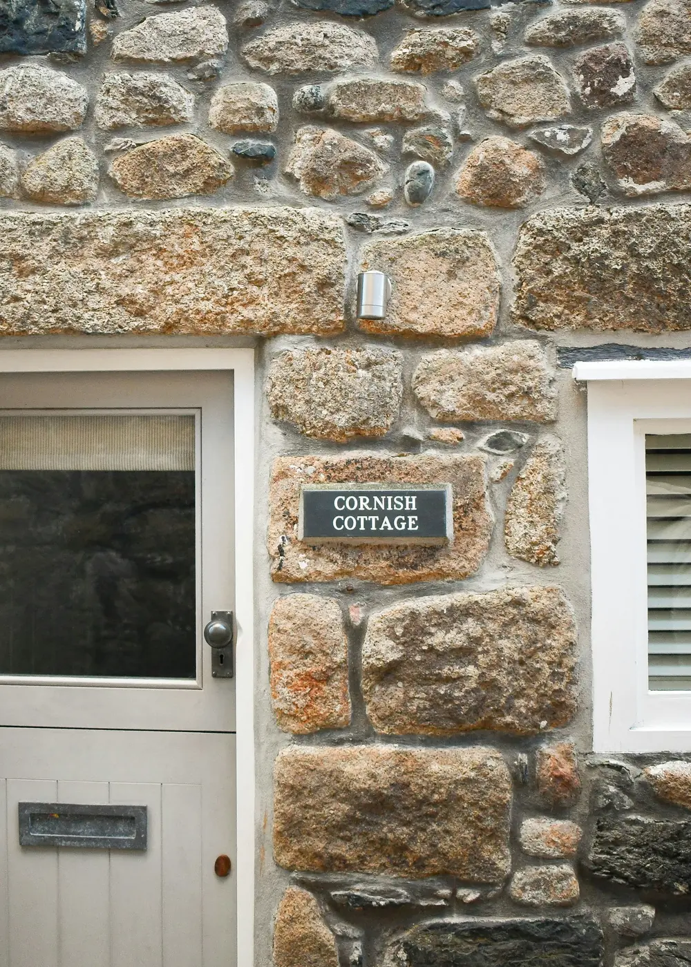 The painted door and granite wall of a Cornish holiday cottage