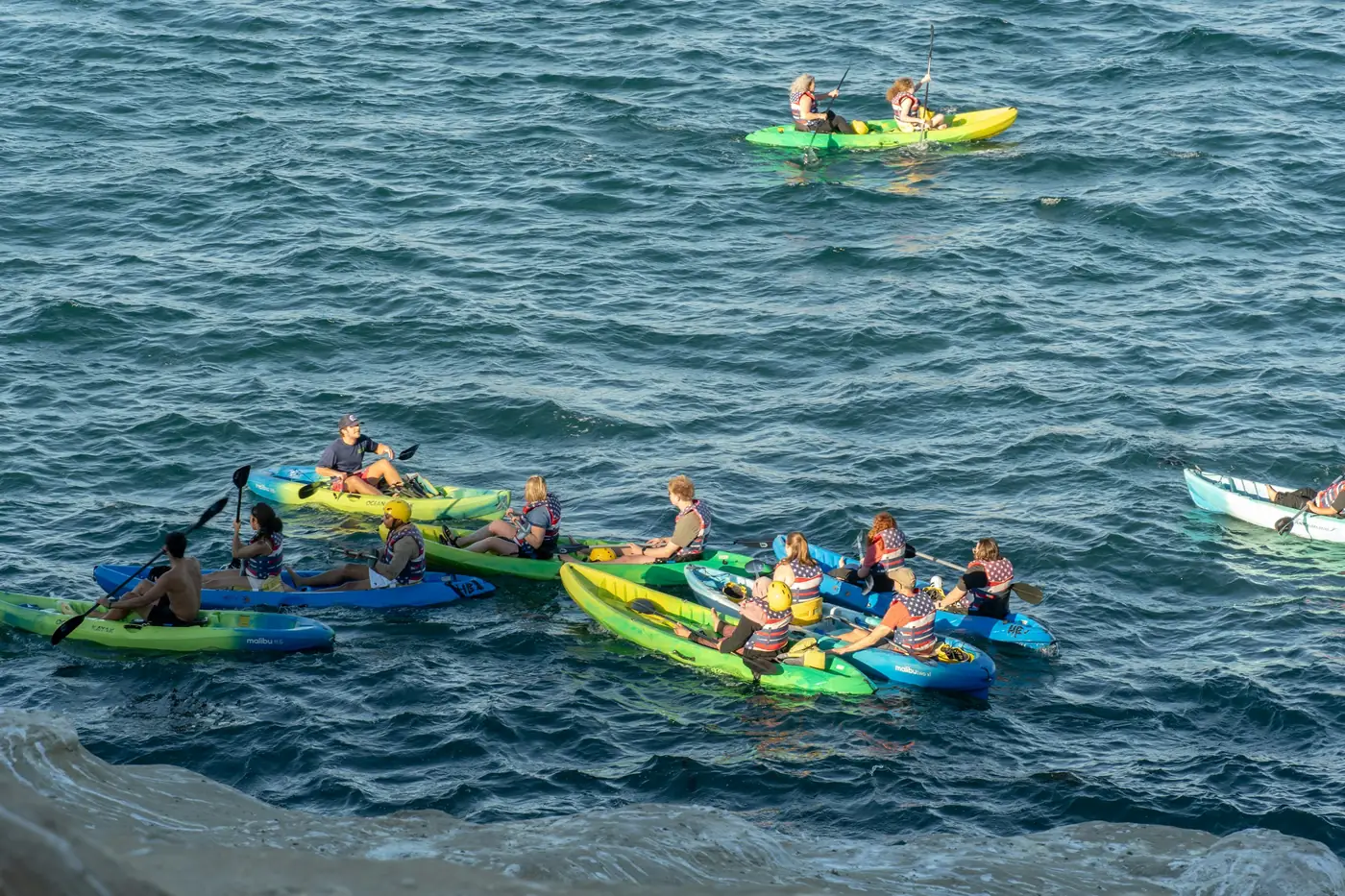 A guided sea-kayaking group paddling together off a rocky coast